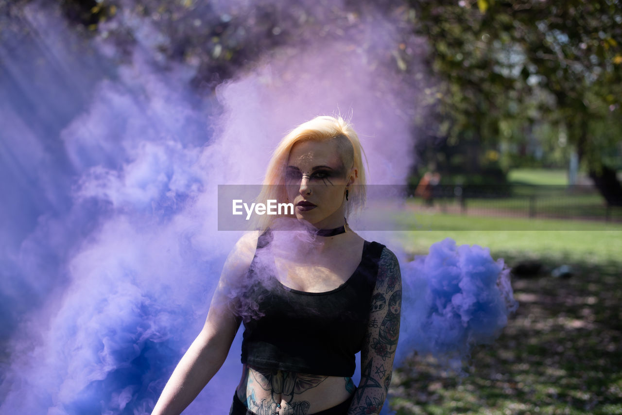 Portrait of woman standing by smoke against trees