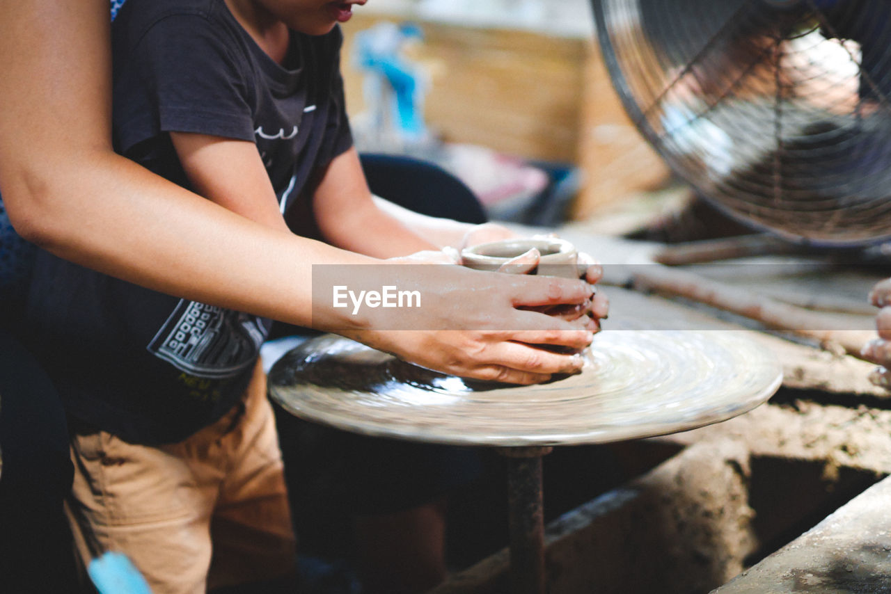 Midsection of people working on pottery wheel