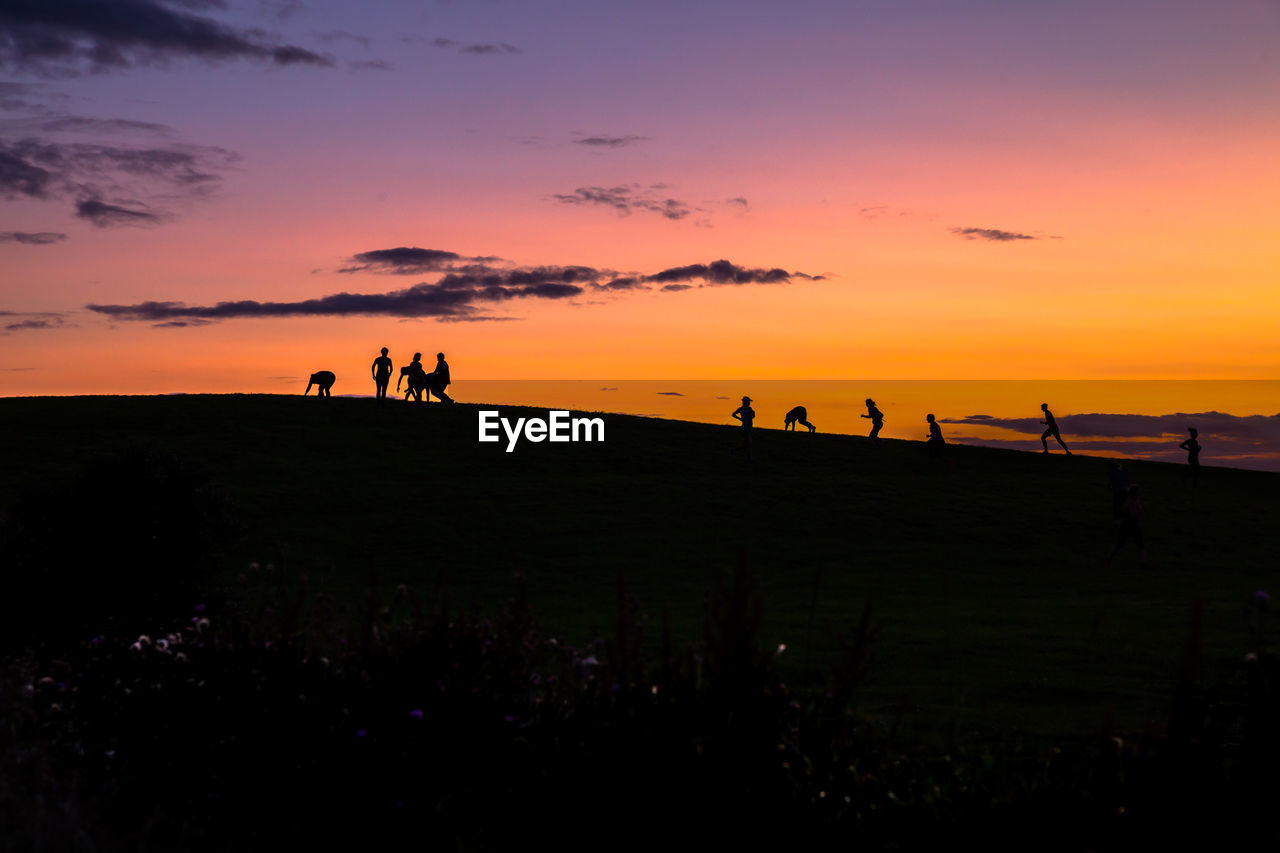 Silhouette people on hills during sunset