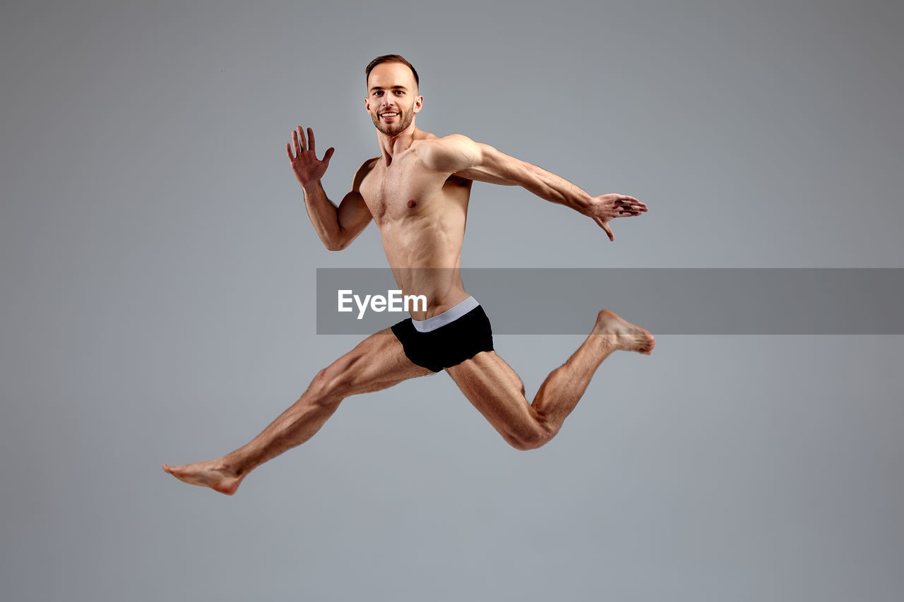 low angle view of shirtless man with arms raised against clear sky