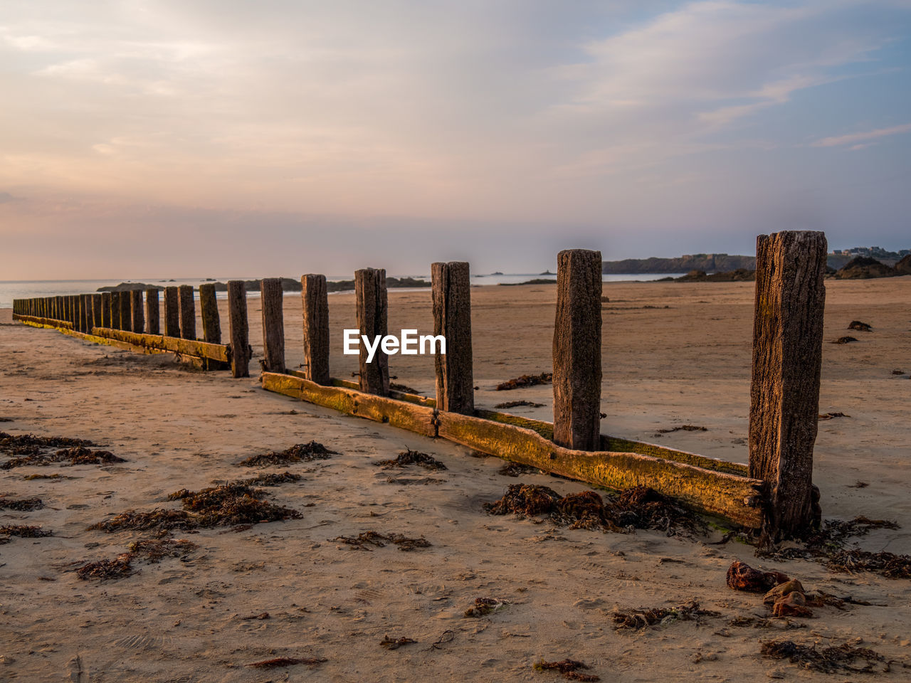 WOODEN POSTS ON BEACH BY SEA AGAINST SKY