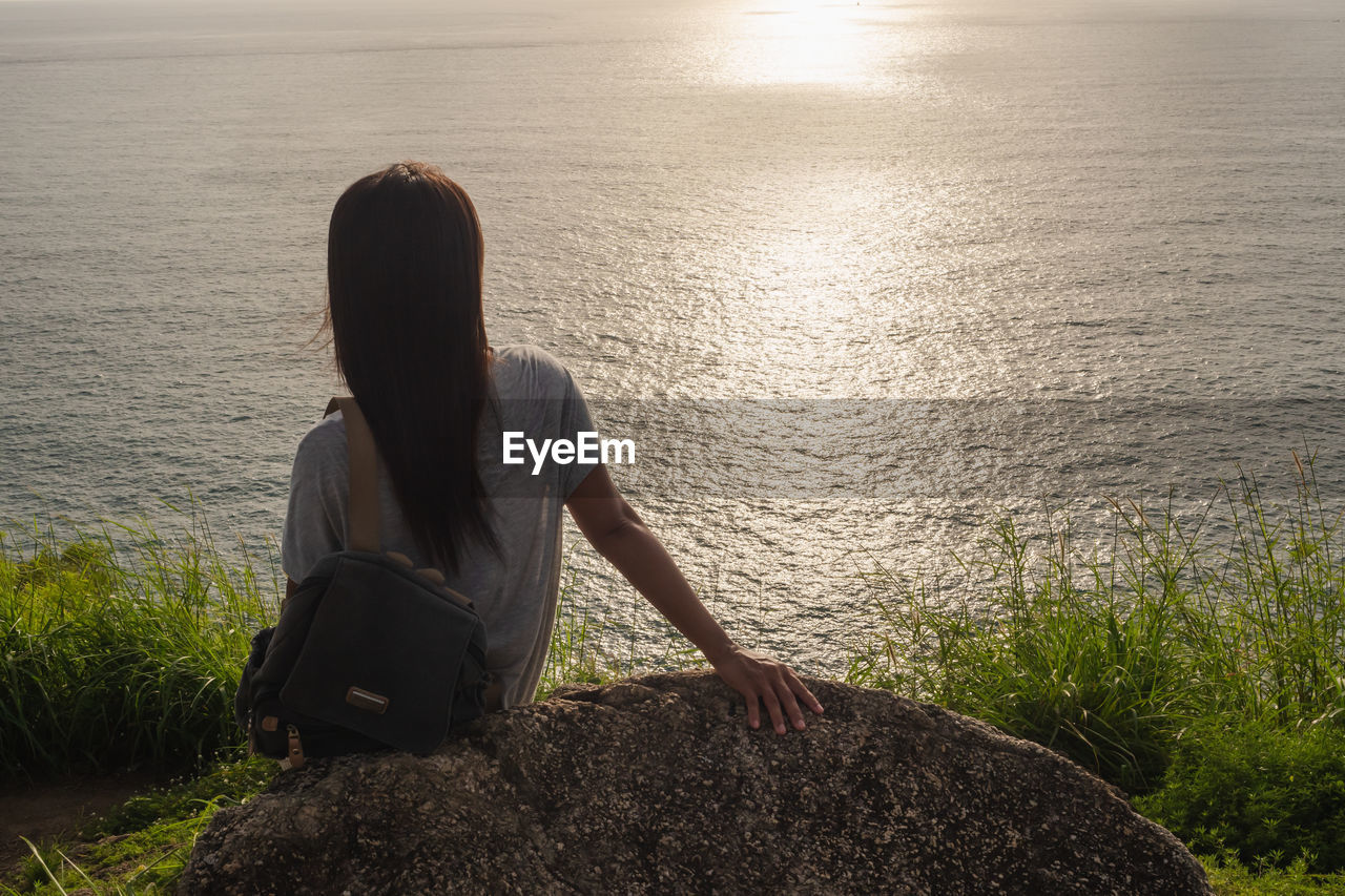 Rear view of woman sitting on rock looking at sea