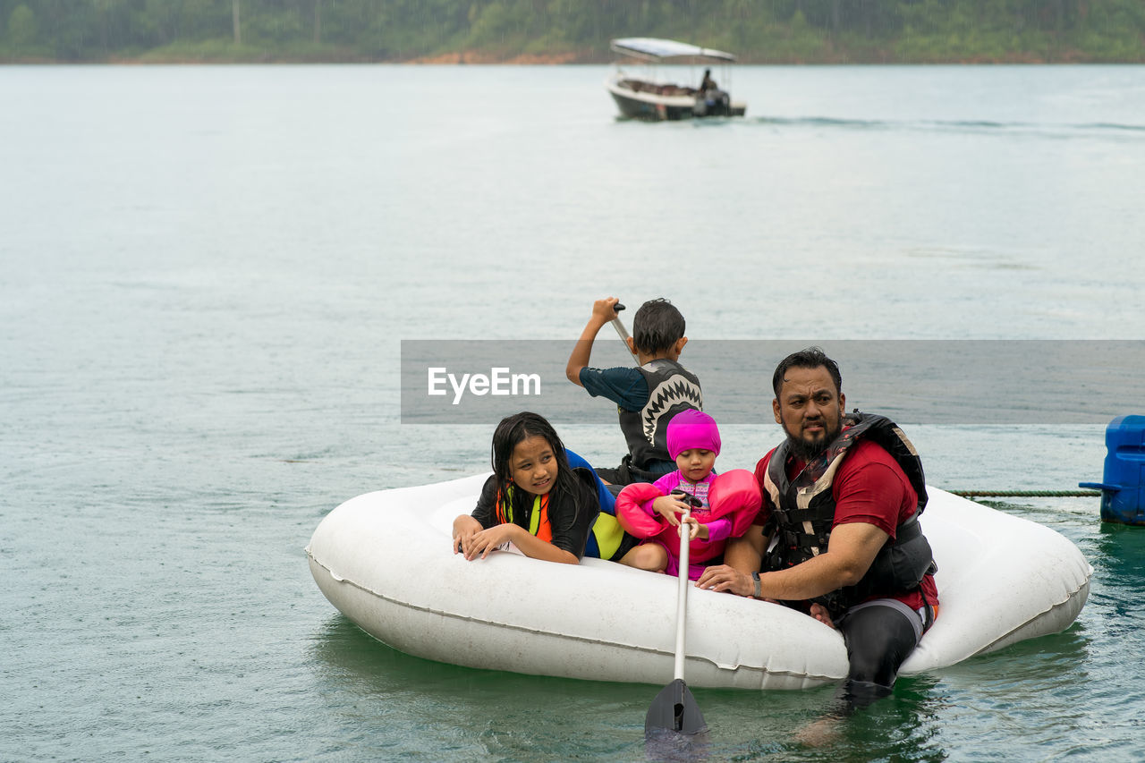 Family wearing life jackets paddling on an inflatable boat in kenyir lake, malaysia.