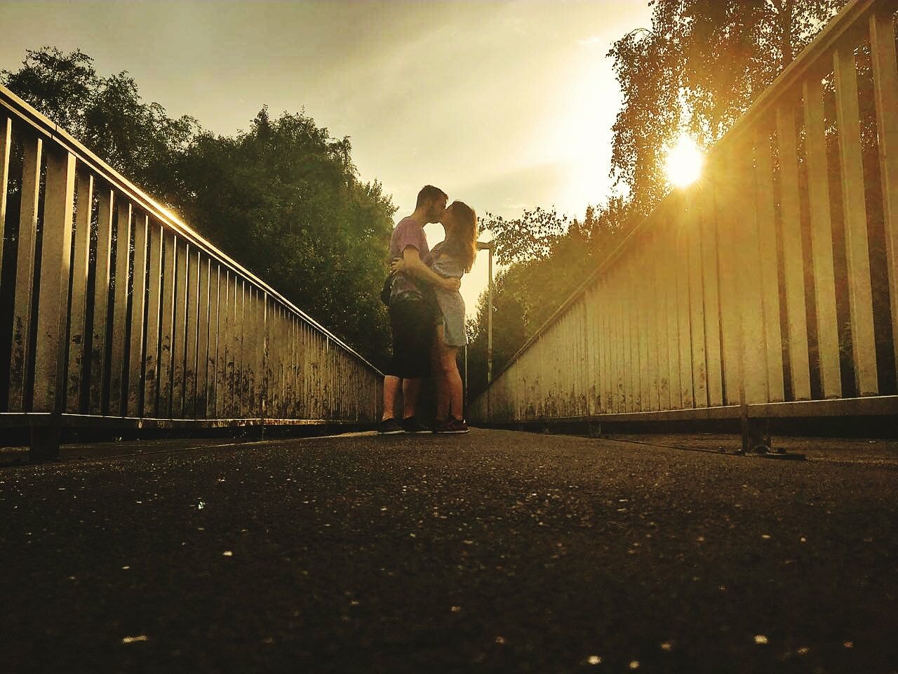 Full length of couple kissing while standing on bridge on sunny day