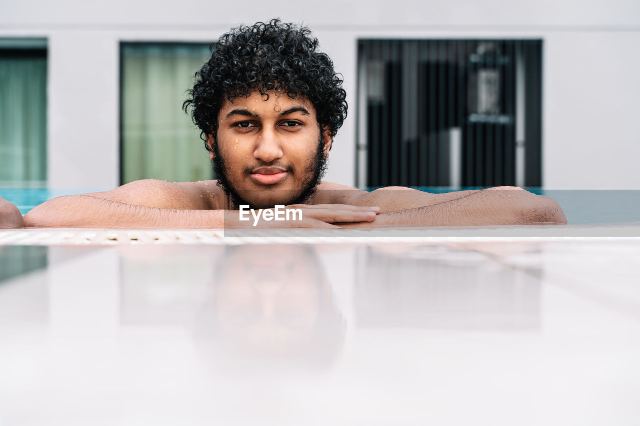Young arabian man with curly hair leaning on the edge of a pool