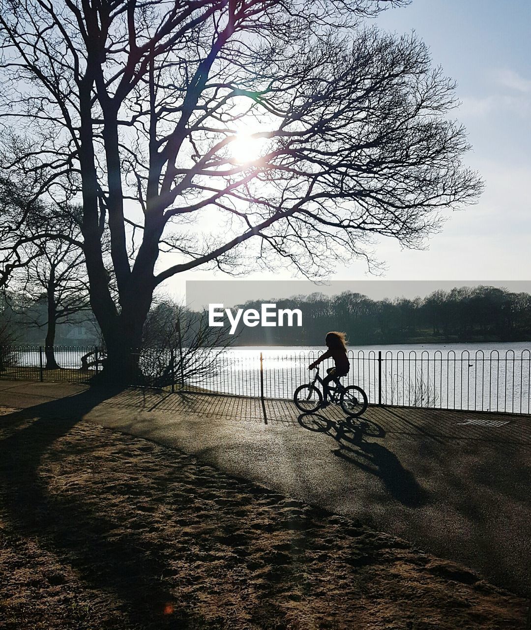 Girl riding bicycle by river against sky