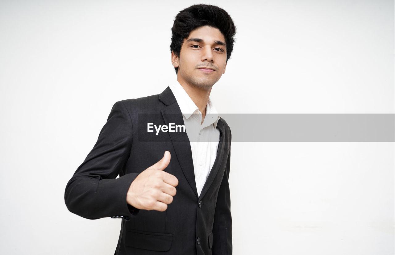 Portrait of businessman showing thumbs up against white background