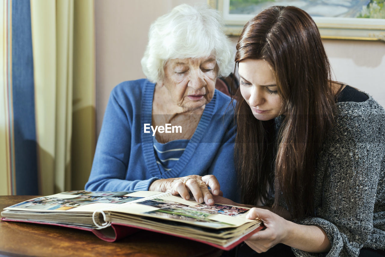 Grandmother and granddaughter looking at photo album in house