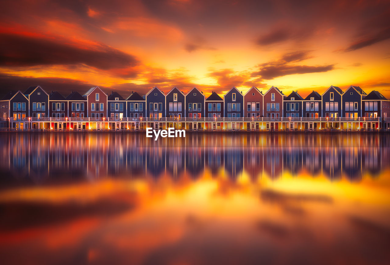 Reflection of buildings on calm lake against orange sky