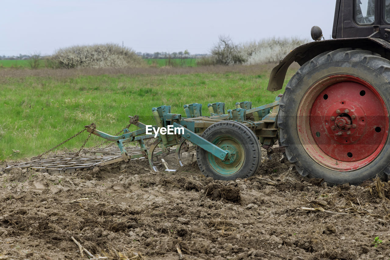 agricultural machinery, soil, tractor, field, transportation, mode of transportation, plough, agriculture, vehicle, land, land vehicle, landscape, rural scene, agricultural equipment, nature, plant, machinery, day, farm, no people, sky, tire, wheel, dirt, environment, grass, outdoors