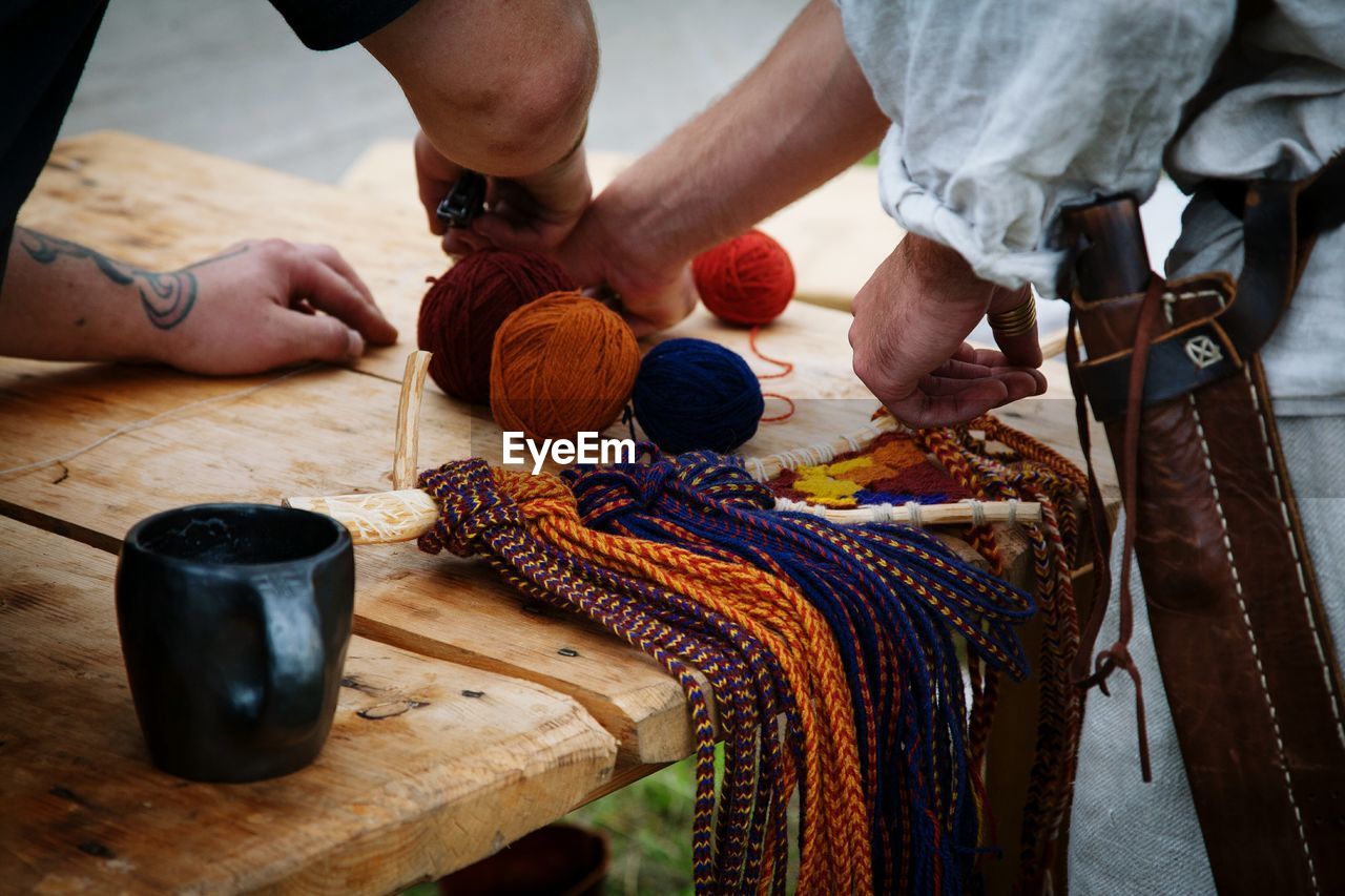 Midsection of men making wool craft product on table