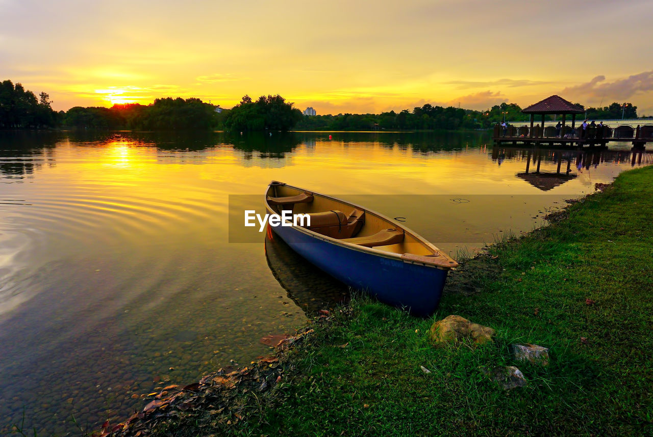 Boat moored on lake against sky during sunset
