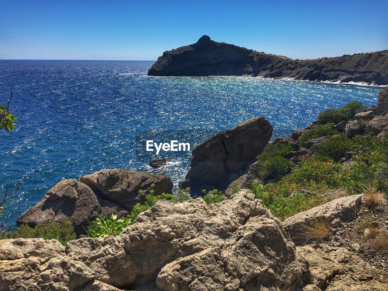 Rocks on shore by sea against blue sky