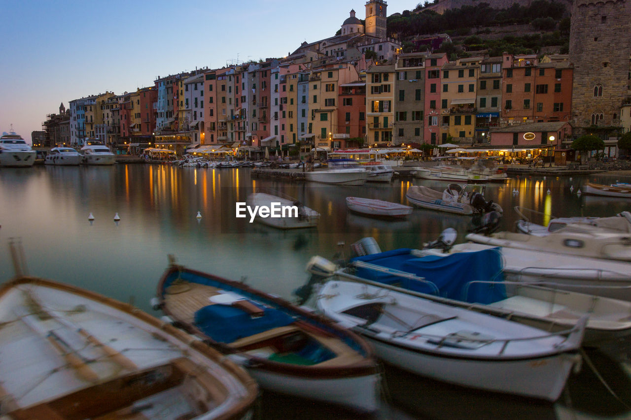 Boats moored at harbor by buildings in city during sunset