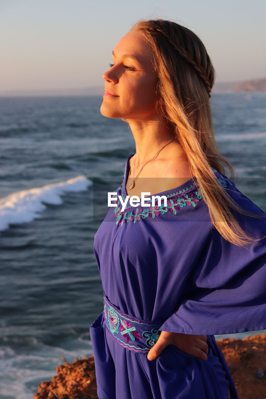 YOUNG WOMAN STANDING AT BEACH