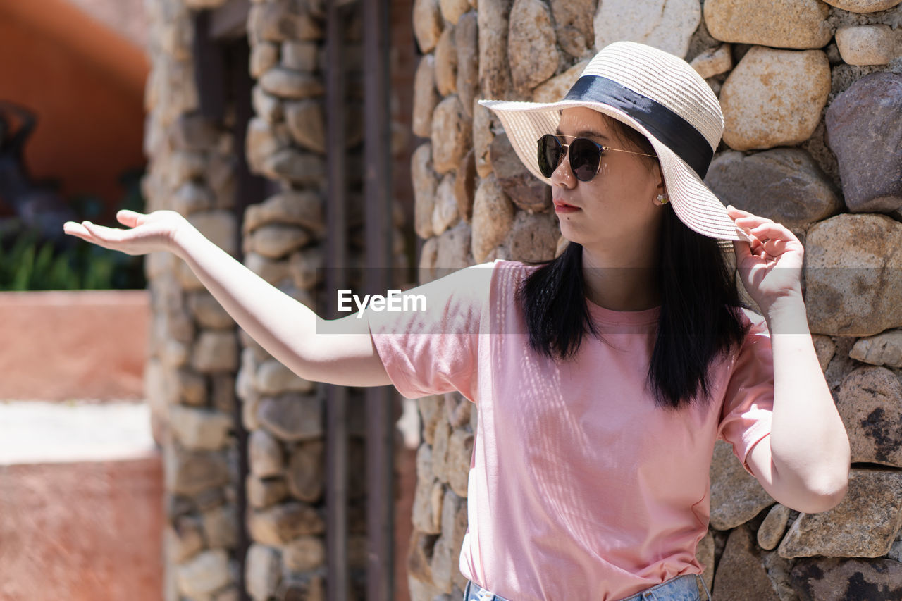 Young woman wearing hat while standing against stone wall