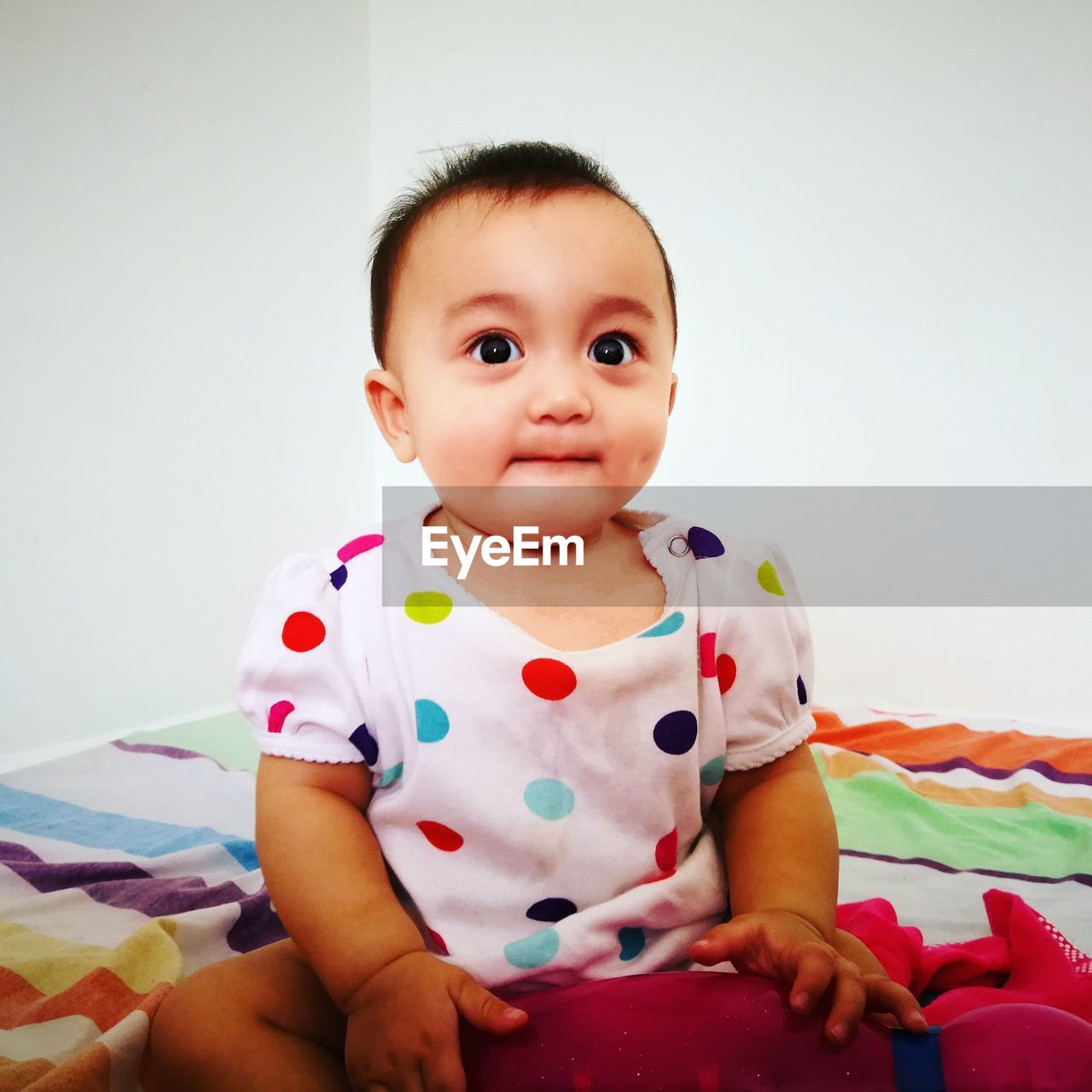 Portrait of cute baby girl sitting on bed