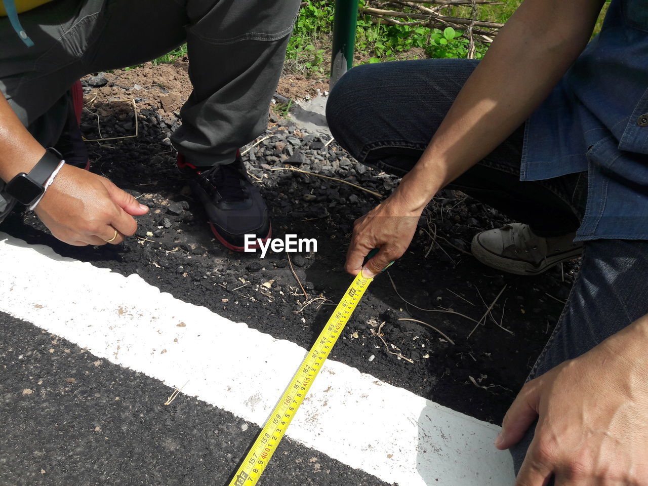 Low section of men measuring road with tape measure