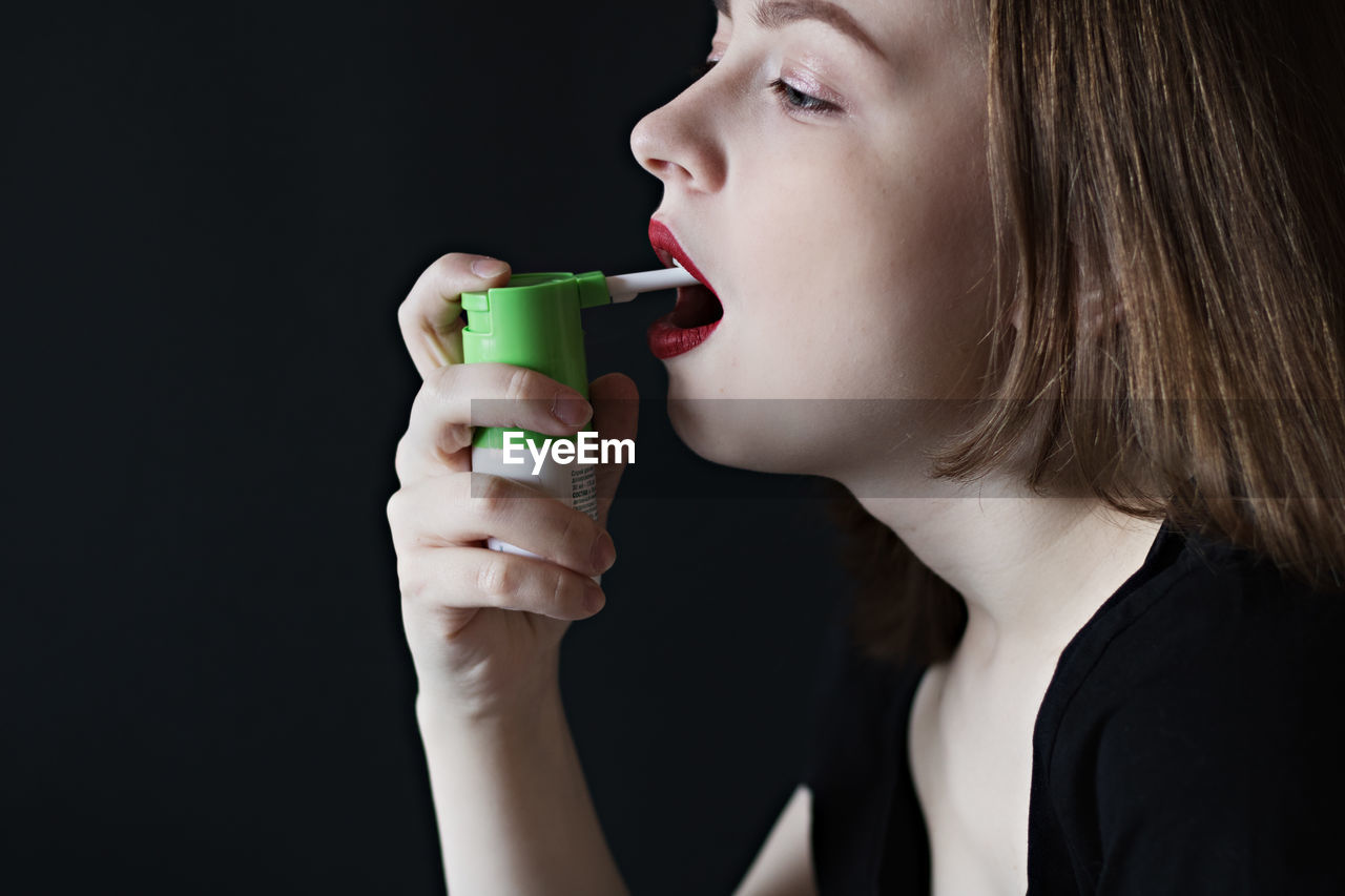 Close-up of woman applying spray in mouth