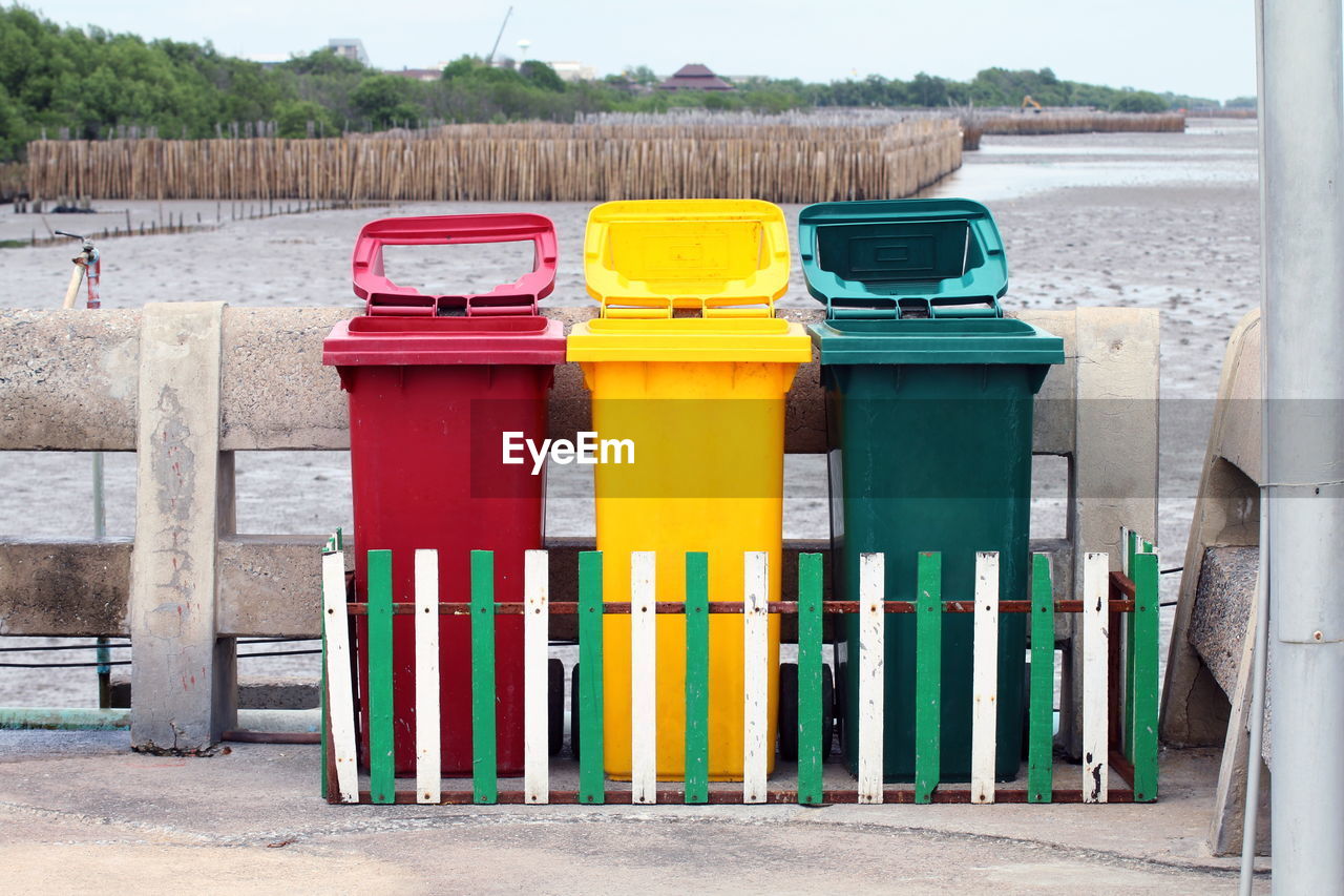 Multi colored garbage bins by fence against field