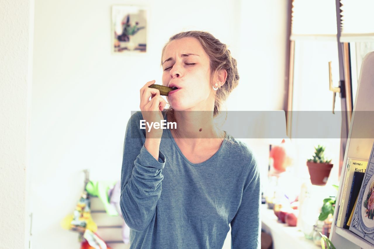 Young woman eating pickled cucumber at home