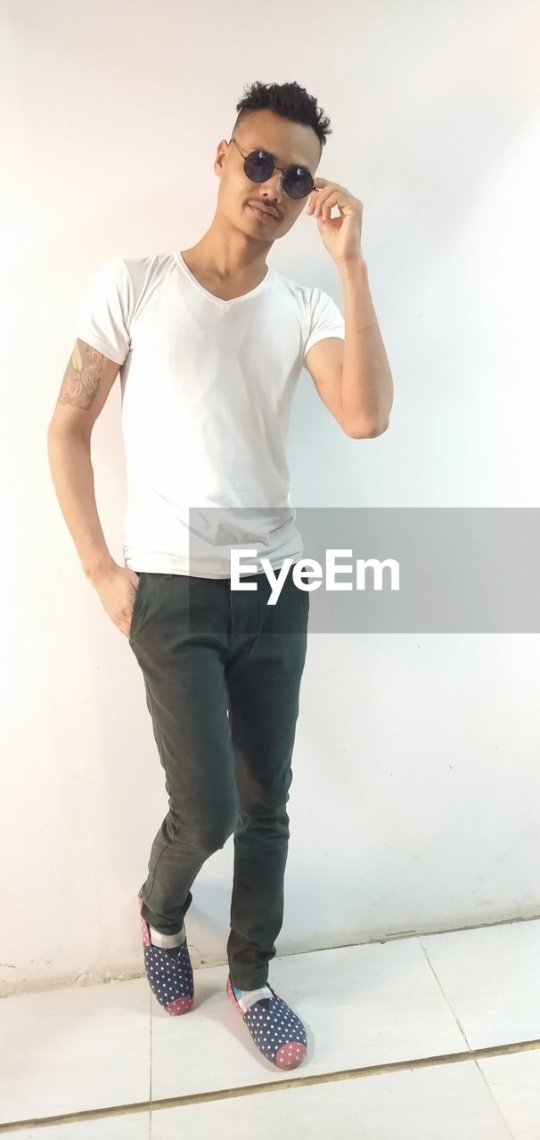 FULL LENGTH OF YOUNG MAN STANDING AGAINST WALL