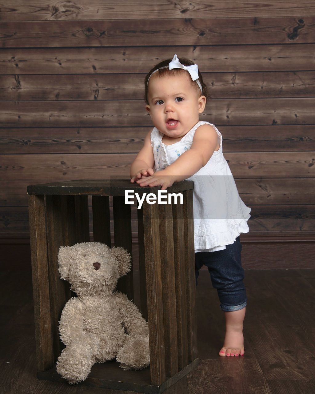 Baby girl standing next to stuffed bear.