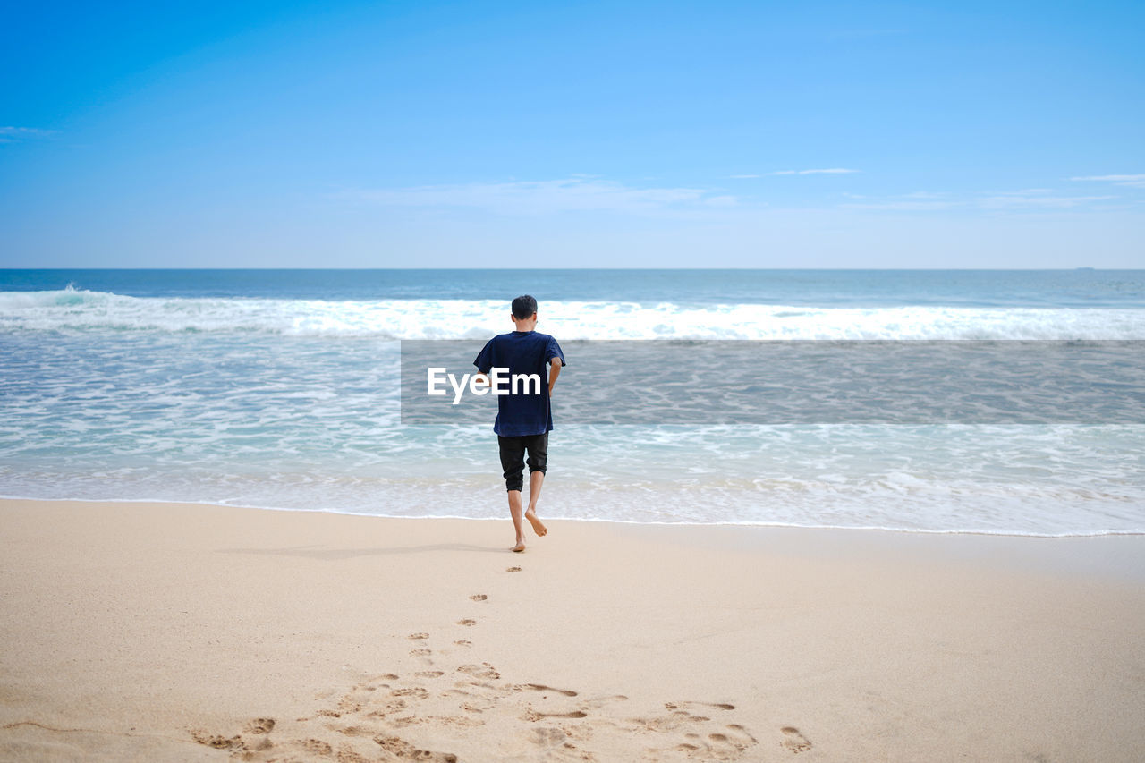 A man in a blue shirt, was approaching the low tide. this beach looks clean and white.