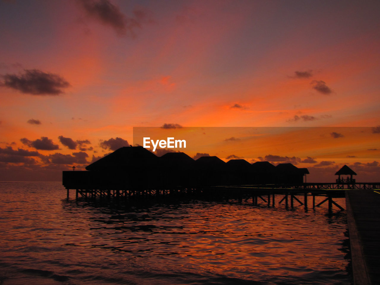 Silhouette pier on sea against orange sky