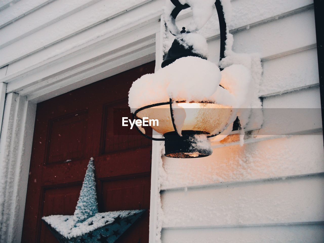 Low angle view of snow covered illuminated lamp mounted on house