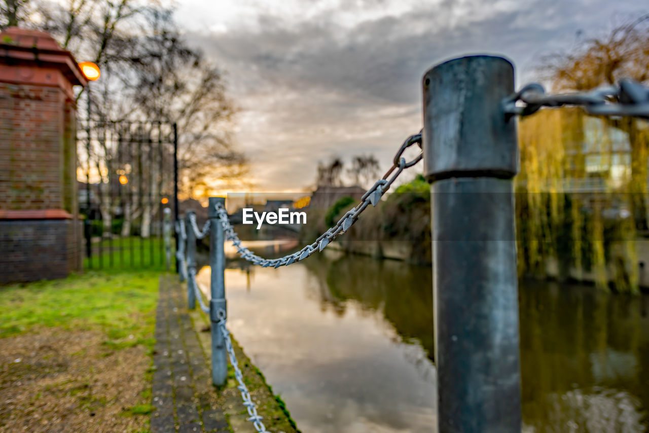 Metal fence by canal against sky