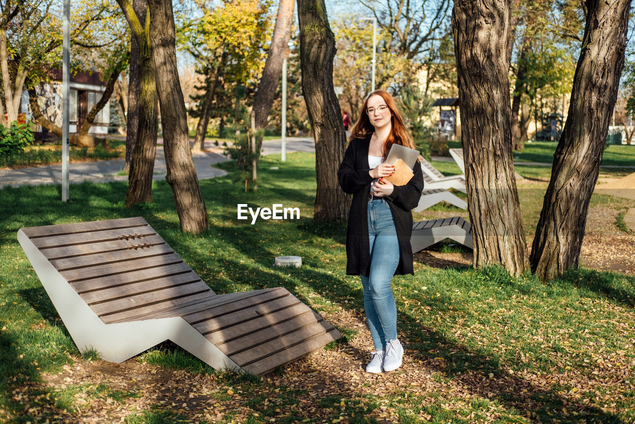 Choosing a university, college. female college student with books and laptop outdoors. redhead