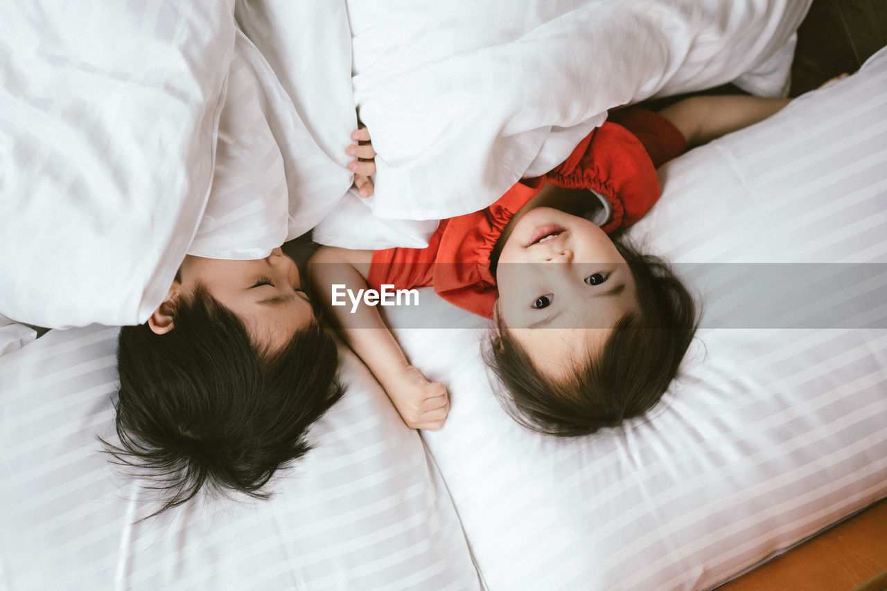 High angle view of siblings relaxing on bed at home