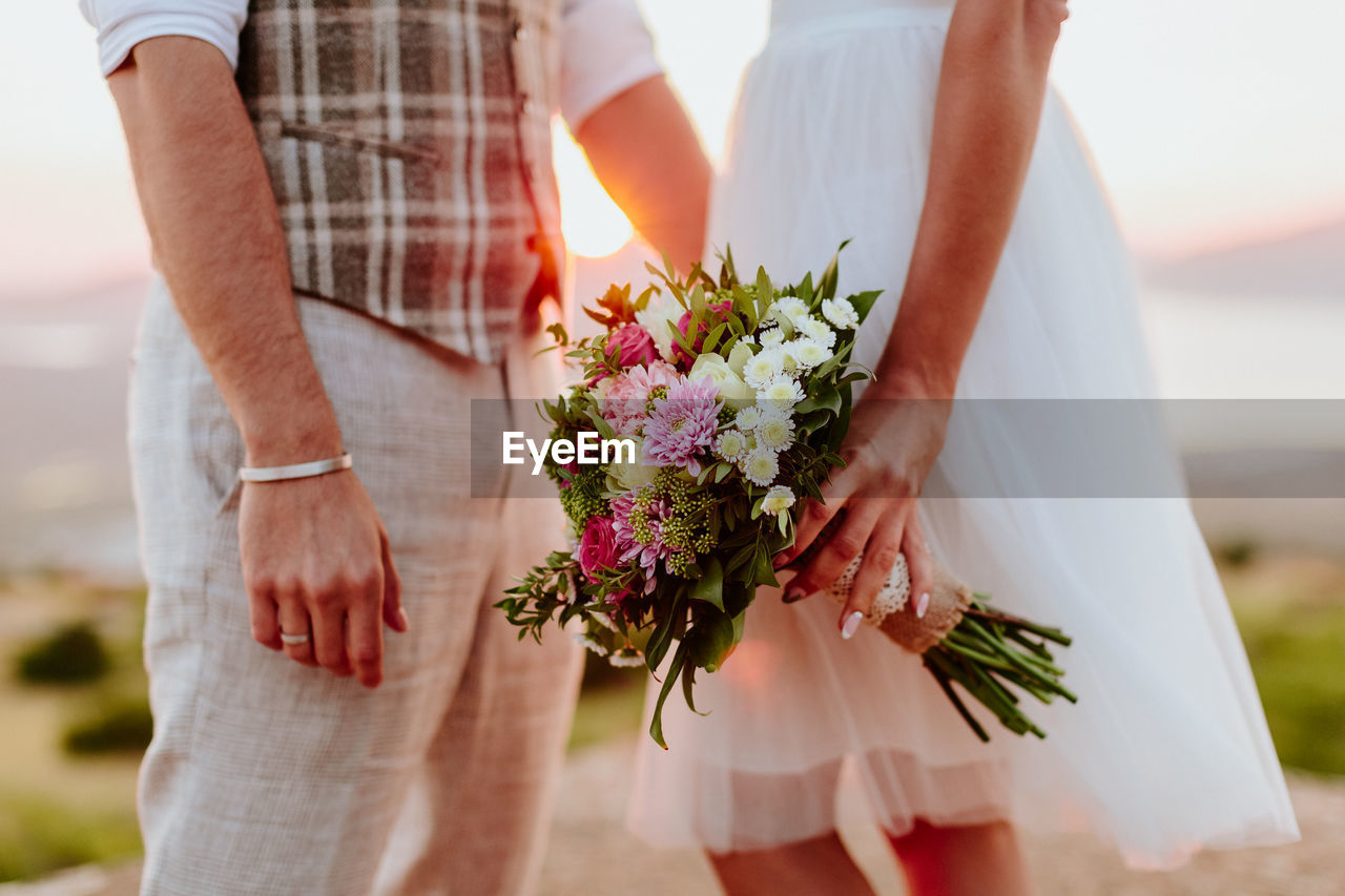 Midsection of bride and groom standing against sky