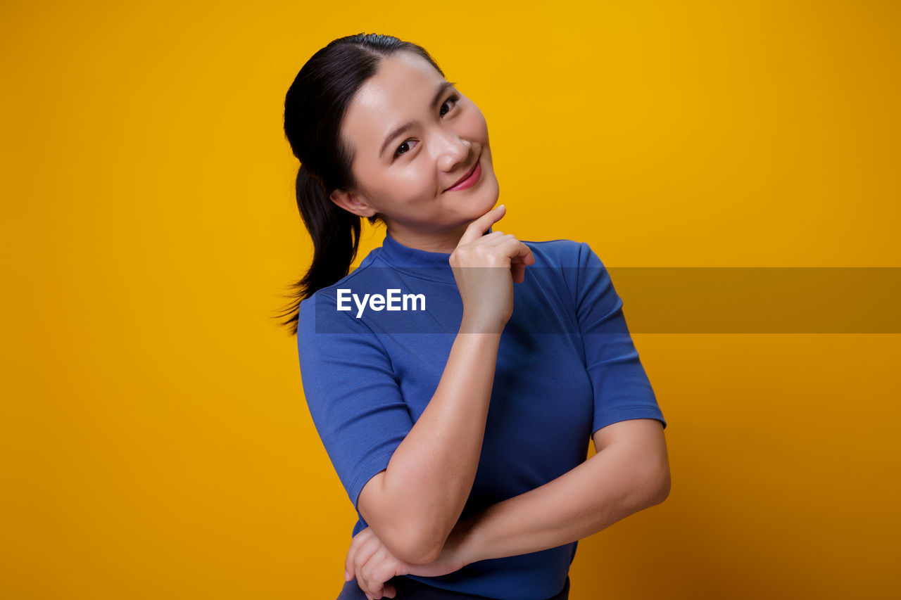 PORTRAIT OF SMILING WOMAN STANDING AGAINST YELLOW BACKGROUND