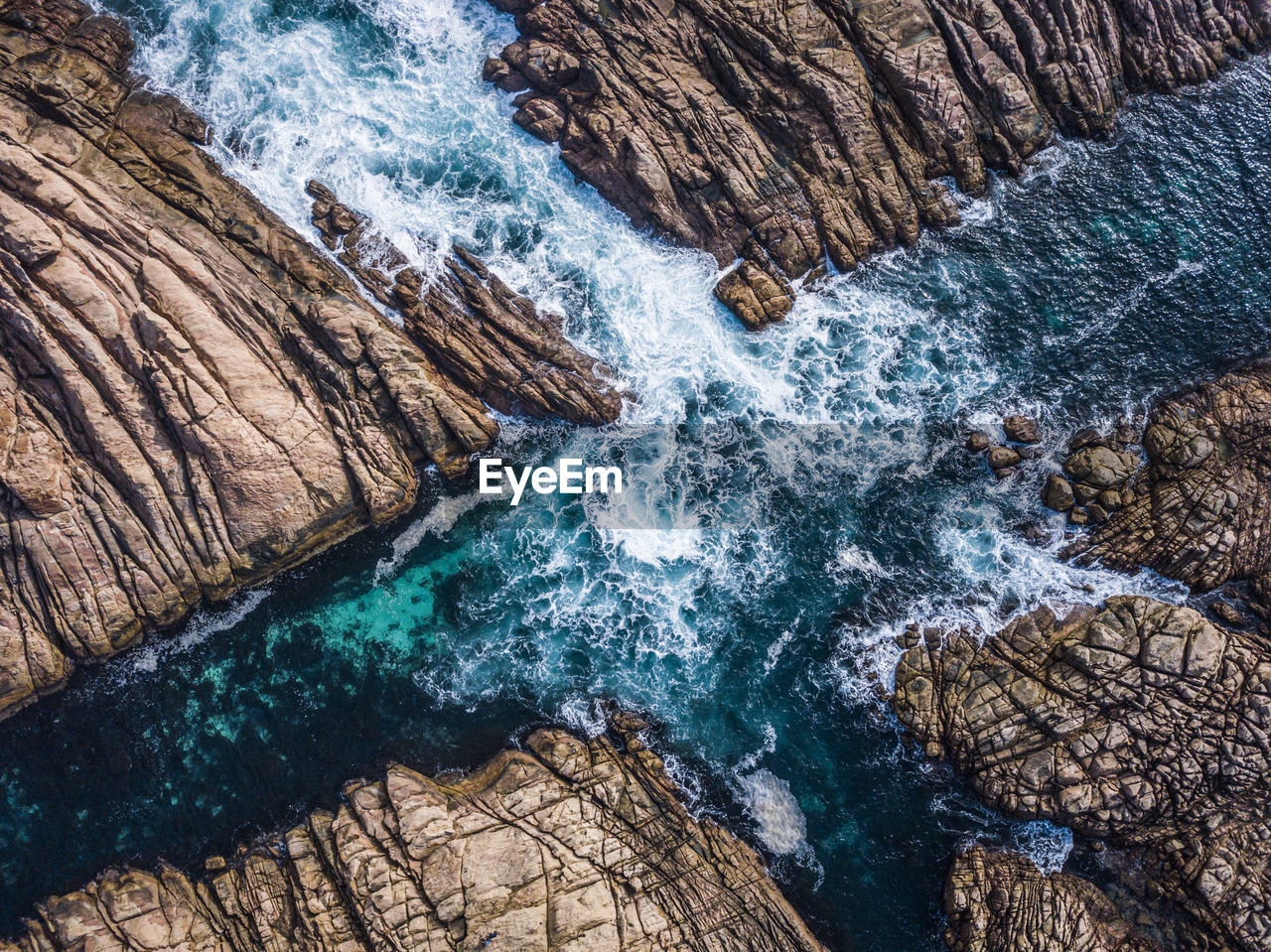 High angle view of waves splashing on rock formations at beach