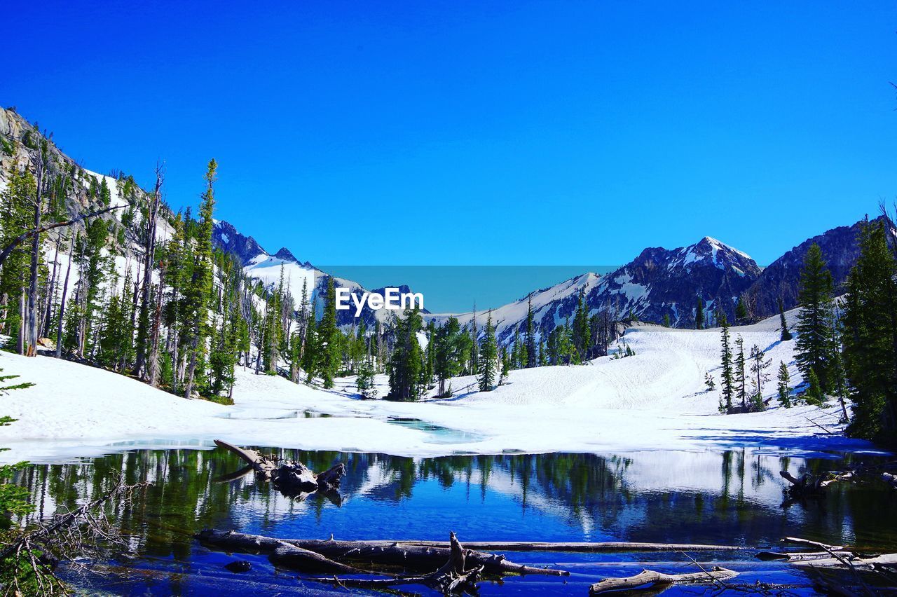 Scenic view of lake and mountains against clear blue sky