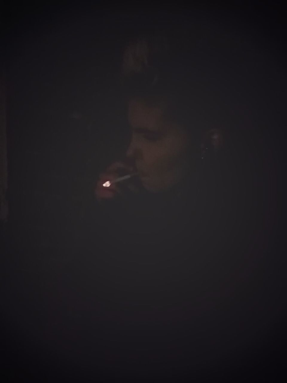 CLOSE-UP OF MAN SMOKING AT BLACK BACKGROUND