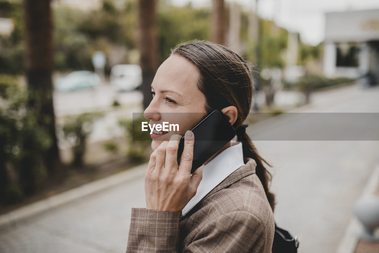 Smiling female professional talking on mobile phone while looking away