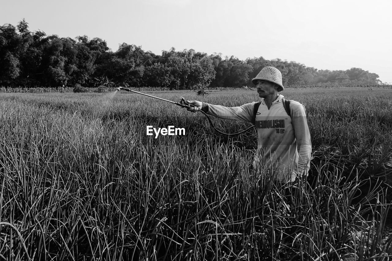 plant, field, black and white, land, one person, adult, rural area, landscape, rural scene, agriculture, nature, crop, monochrome photography, growth, hat, grass, sky, monochrome, farm, men, environment, occupation, farmer, cereal plant, day, clothing, prairie, lifestyles, outdoors, working, tranquility, cap, paddy field, person, three quarter length, tree