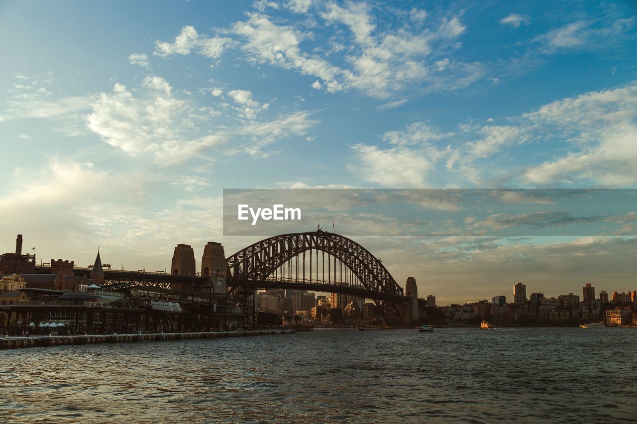 Bridge over river against sky in city during sunset