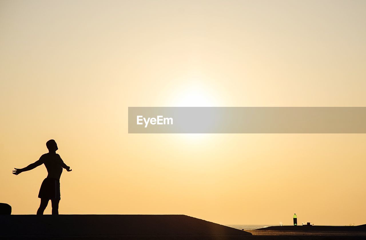 Silhouette man with arms outstretched standing at beach against sky during sunrise