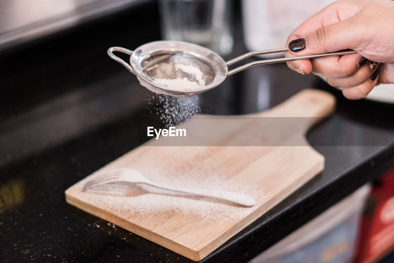 Cropped hand of woman holding sieve in kitchen