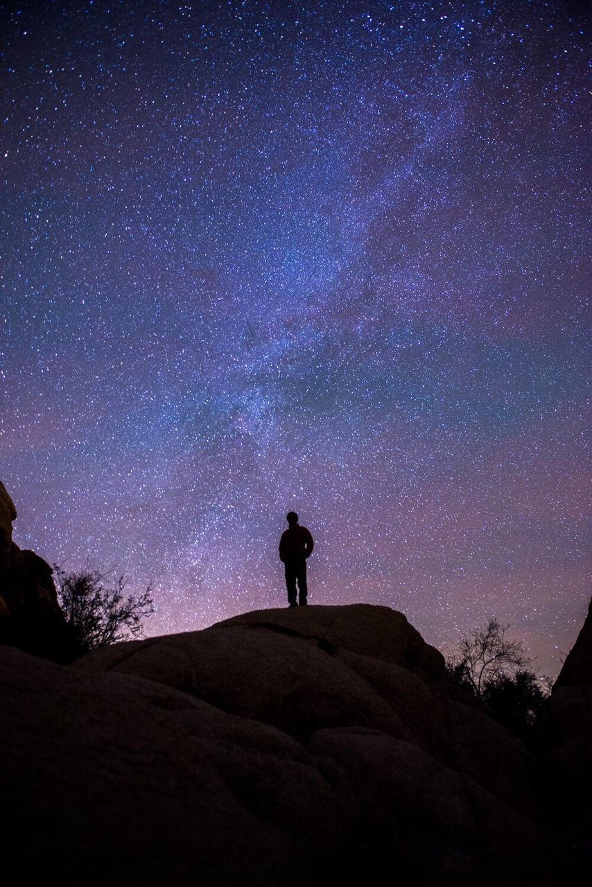 Low angle view of silhouette man standing on rocky mountains against star field at night