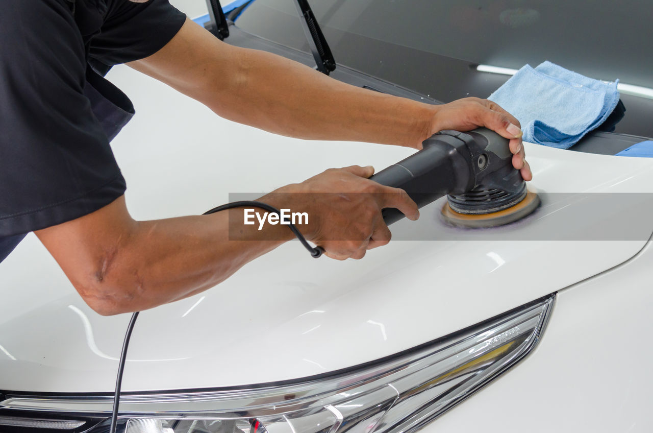 Cropped hands of mechanic polishing car in garage