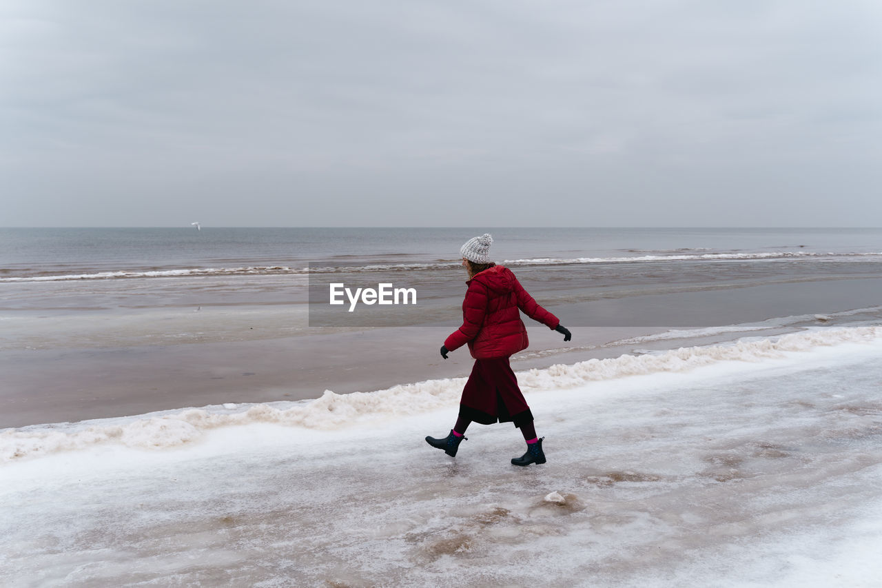 A woman in red walks in winter along the seashore