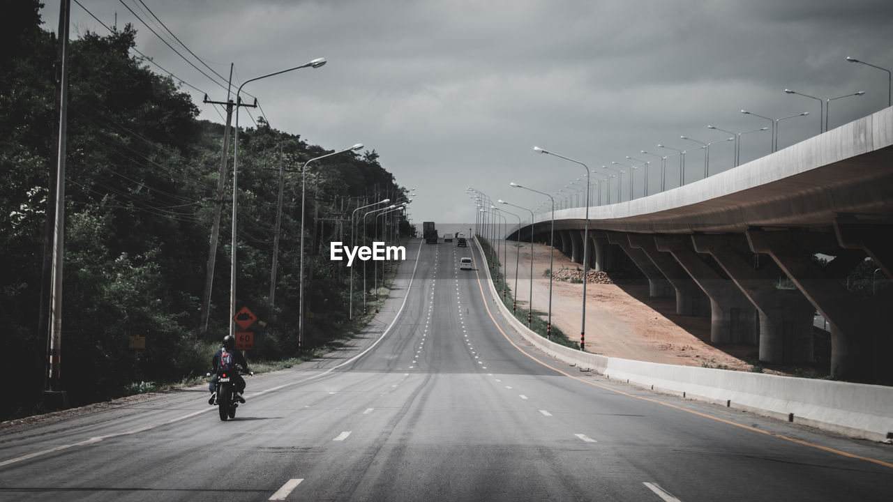 MAN RIDING BICYCLE ON BRIDGE AGAINST SKY