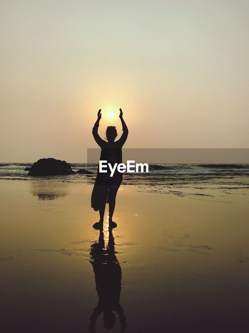 Optical illusion of silhouette woman holding sun while standing at beach