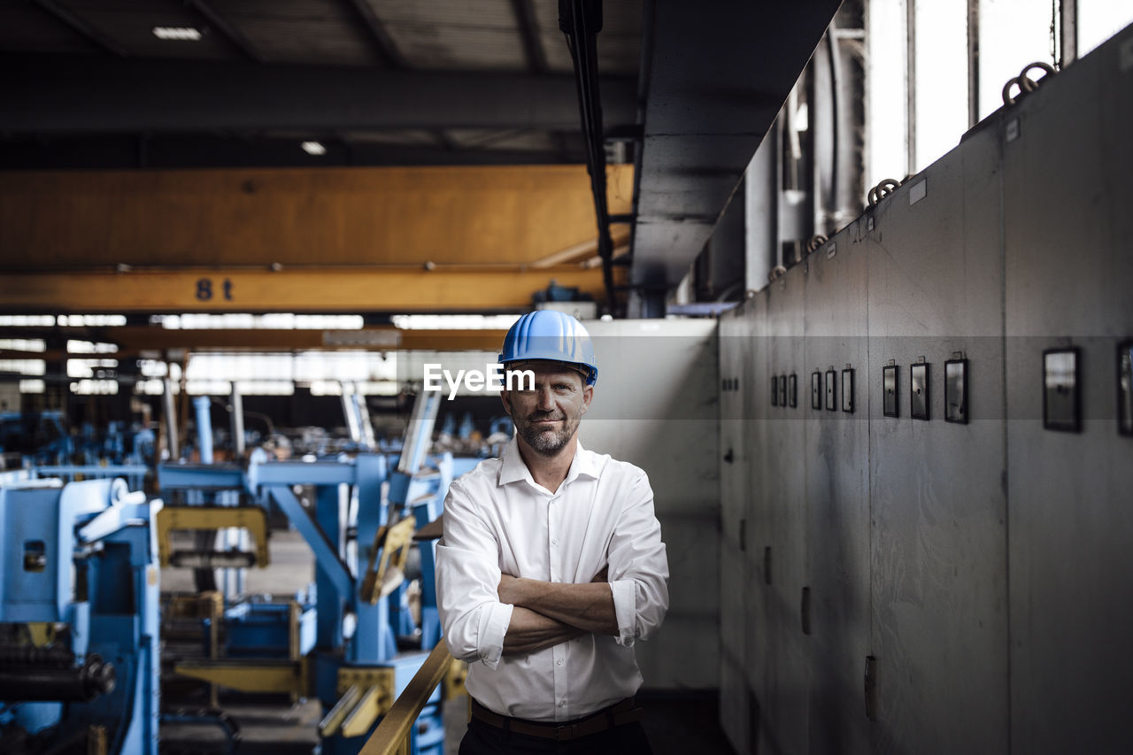Smiling businessman with arms crossed standing in factory