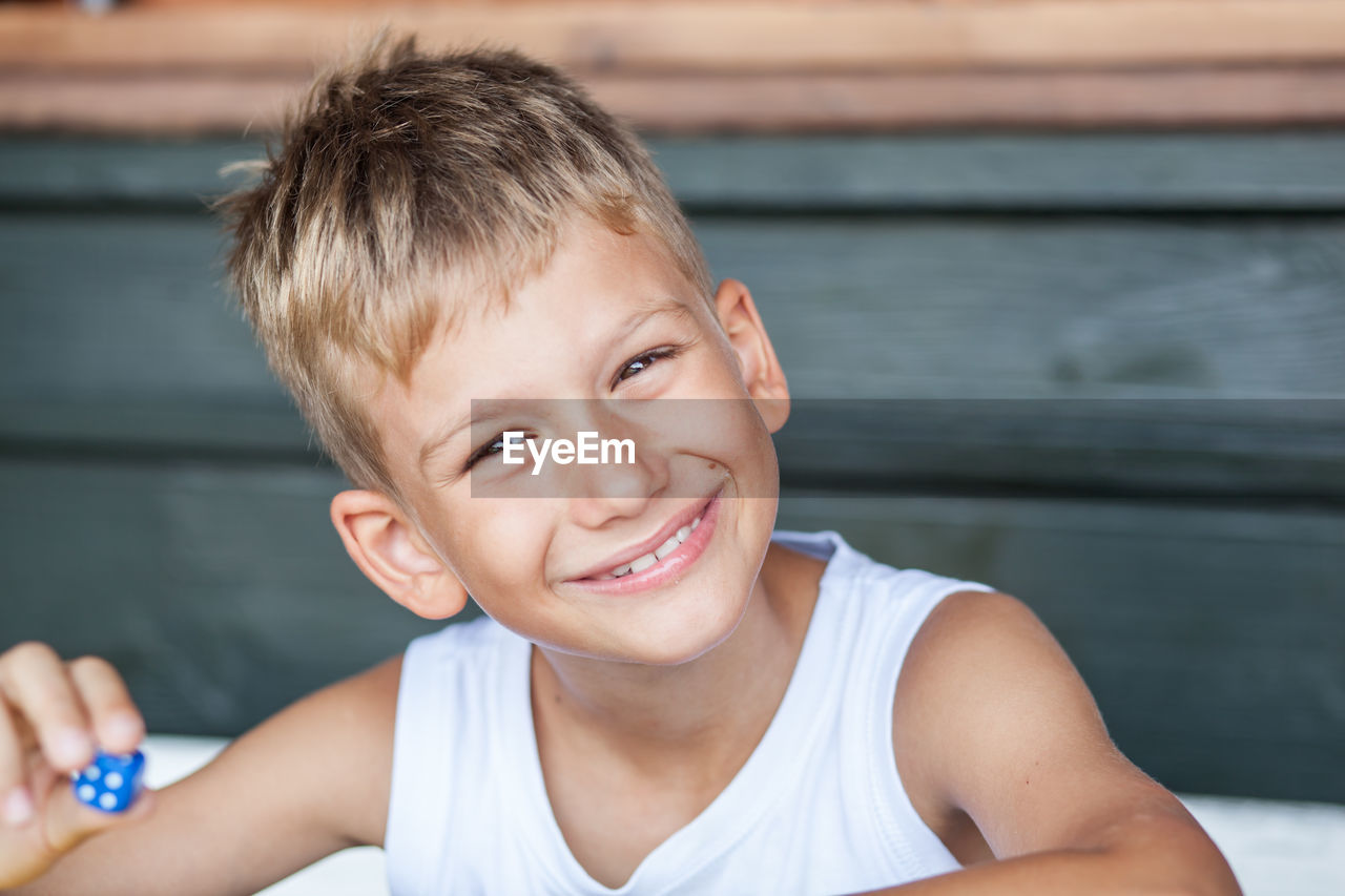 Portrait of smiling boy holding blue dice at home